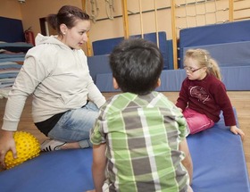 Kinder mit Betreuerin auf einer Turnmatte