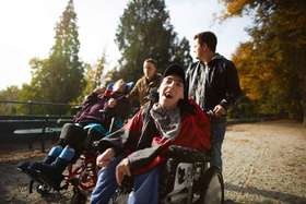 Betreuer mit Männern im Rollstuhl beim Spatziergang